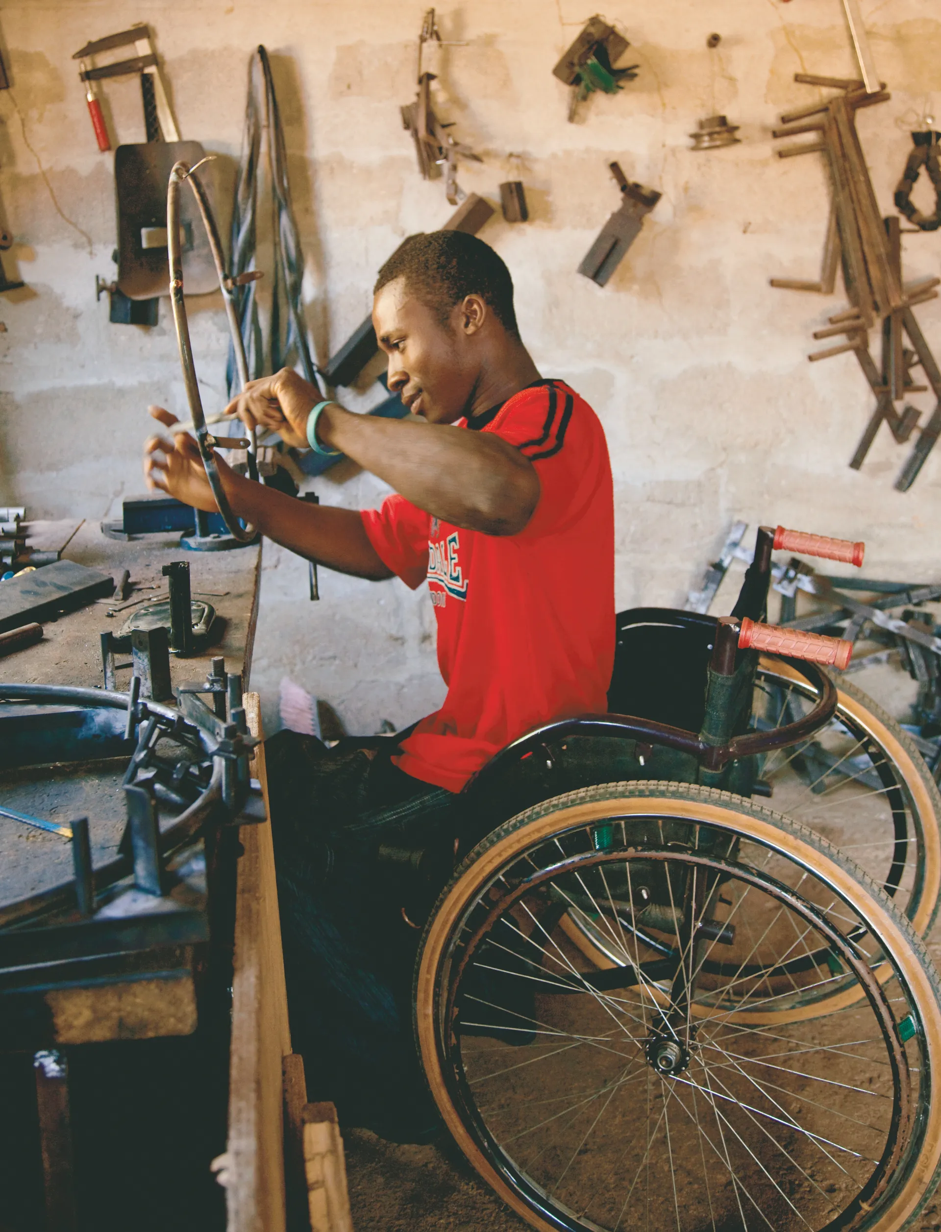 A man from Africa sitting in a wheelchair, repairing another wheelchair part.
