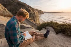 A young man reads the scriptures on a beach