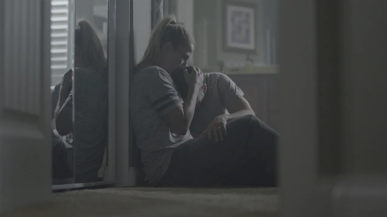 A mother sits in a kitchen comforting her son