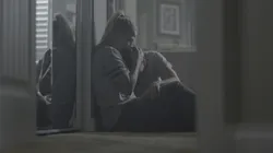 A mother sits in a kitchen comforting her son