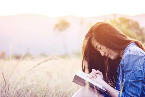 woman praying in meadow at sunset