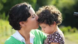 A mom kissing her daughter on the forehead
