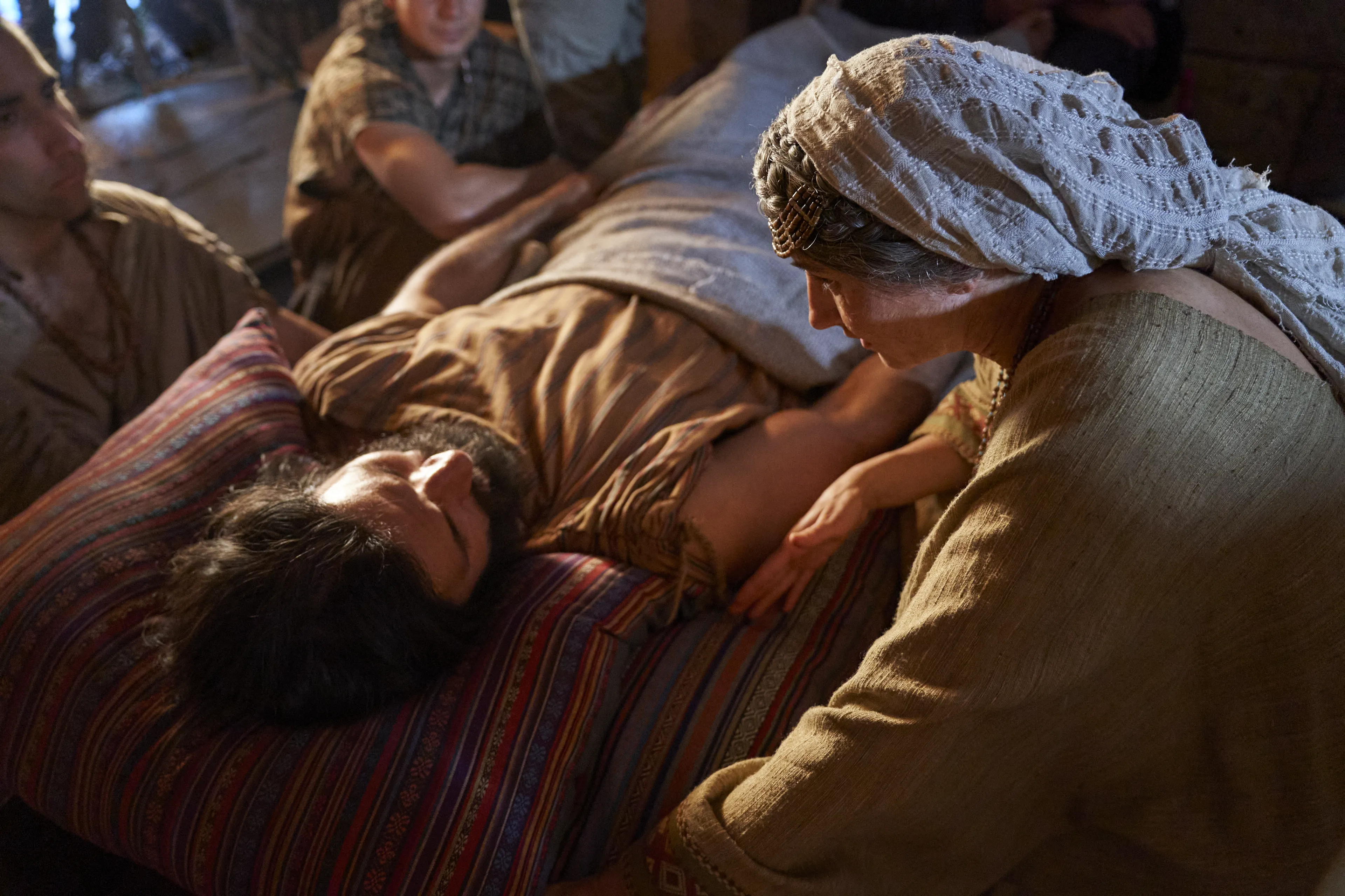 Alma the Younger lies on his bed struck dumb, while his mother and priests look on.