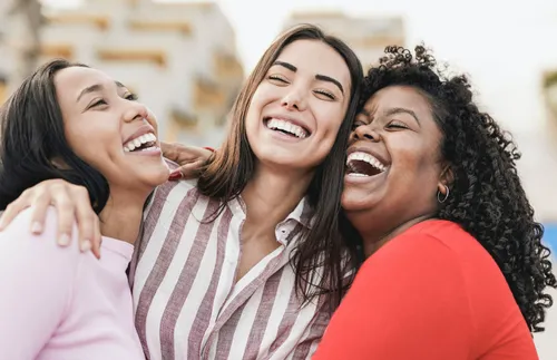 three women stand together and laugh
