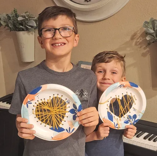 Two boys holding hearts made from paper plates and yarn