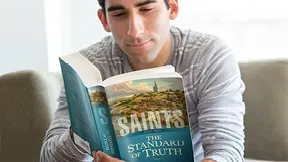 A man is holding up a book and reading it. There is text on the banner.