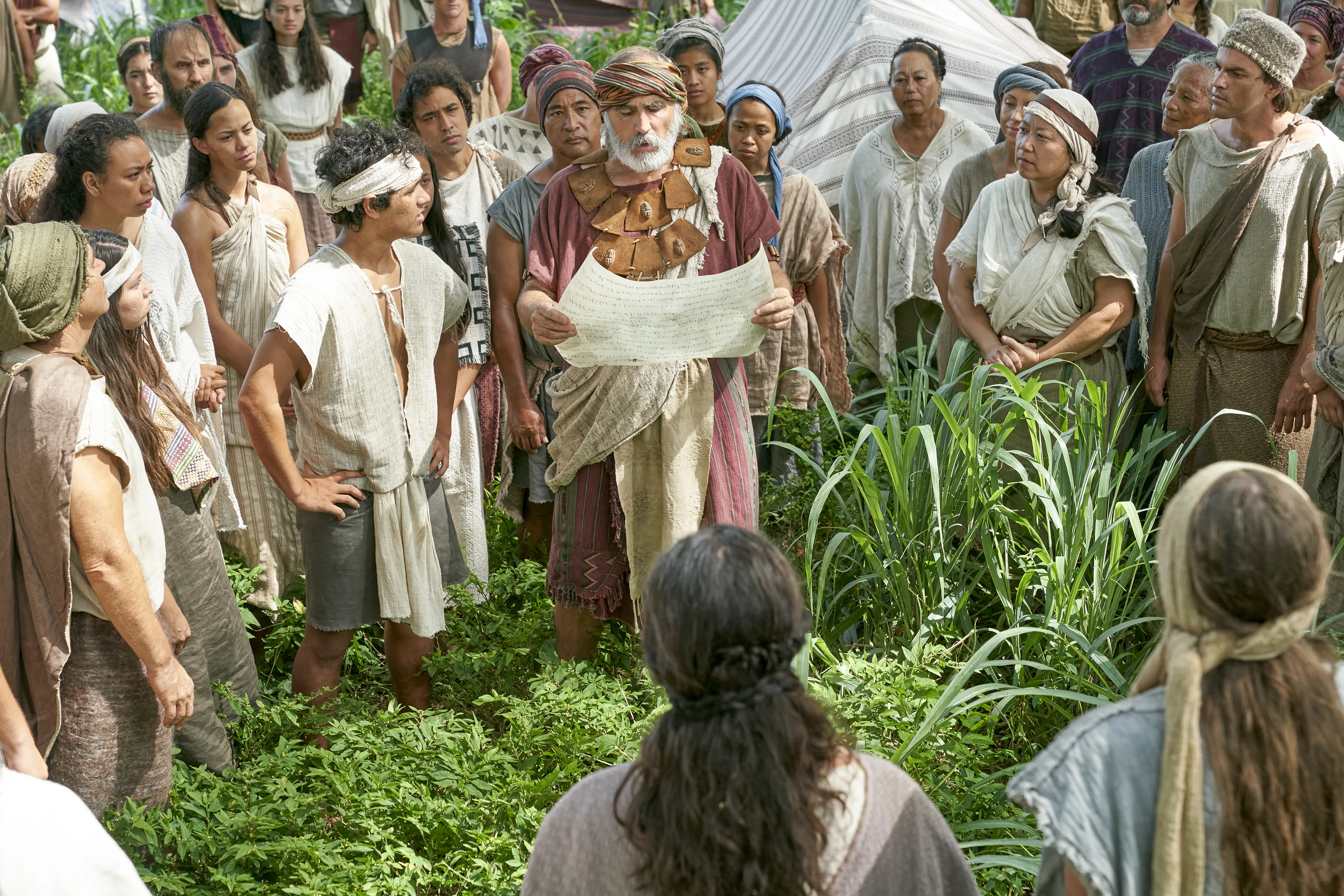 Men and women gather to listen to the teaching of King Benjamin as they are read from a parchment in the Land of Zarahemla.