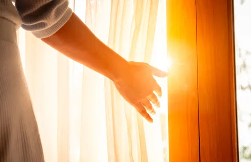a hand opening a curtain and letting light in