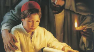 Jesus Christ depicted as a young boy in the carpenter shop of Joseph. Joseph is standing behind the young Christ.  Christ is reading the scriptures from a scroll resting on a table. There are wood shavings on the table.
