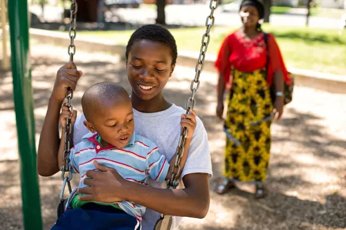 Young boy sitting on the lap of an older boy as they swing.