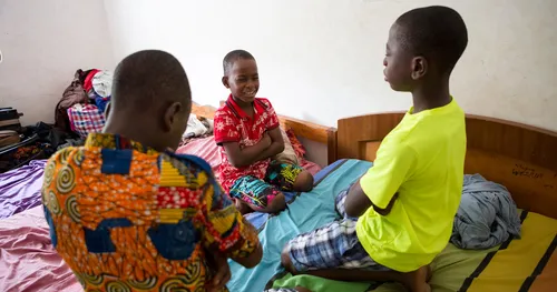 Three boys in Ghana kneel on their beds while bowing their heads in prayer.