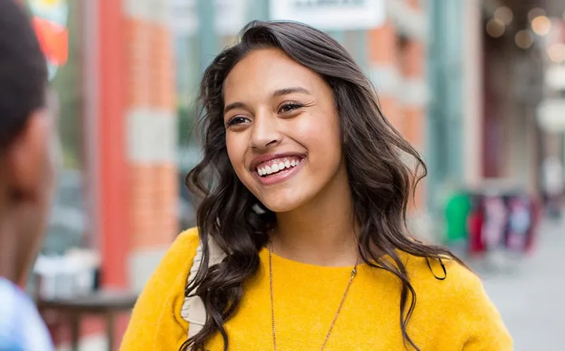 A woman in a yellow sweater smiling as she talks to someone