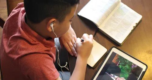young man taking notes while watching general conference on a tablet