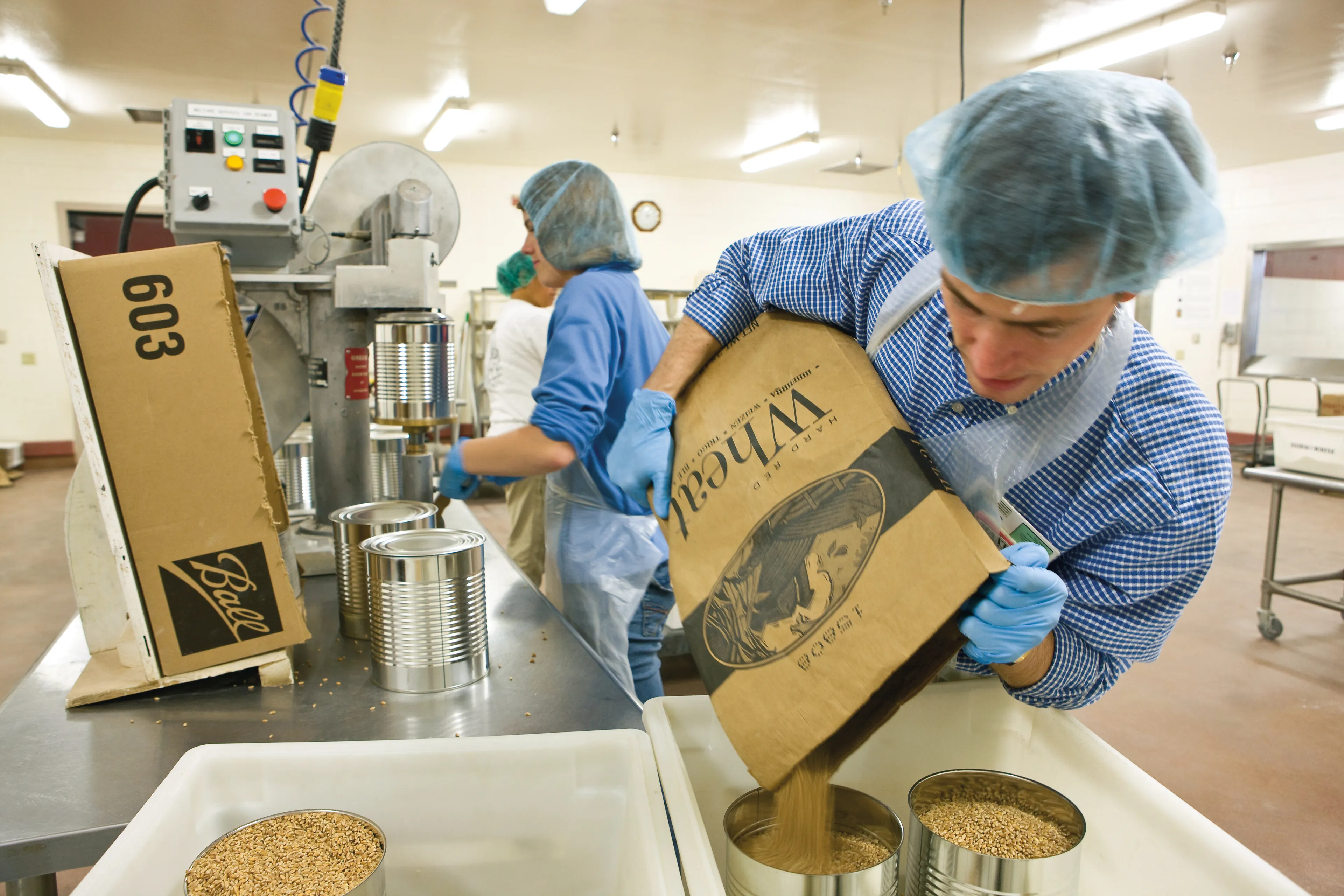 A man pouring wheat into large cans at the cannery.