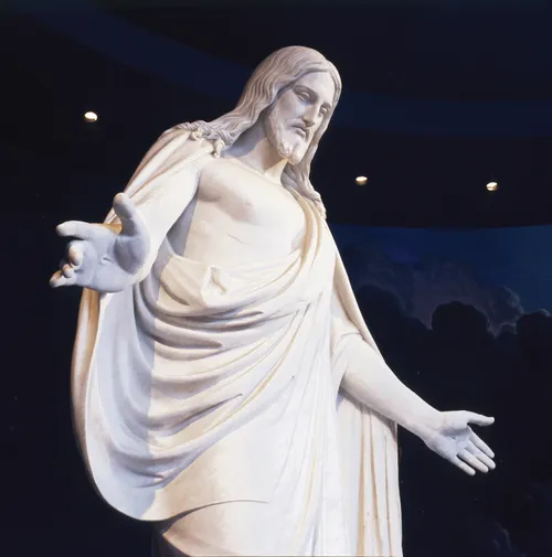 A white statue of Jesus Christ with arms outstretched, surrounded by a mural of blue sky.