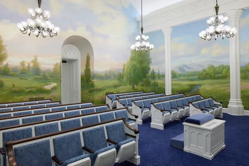 Interior image of the St. George Utah Temple. The image features the Instruction Room (Ordinance Room). It features an altar in the front, murals of the area, and chairs. 