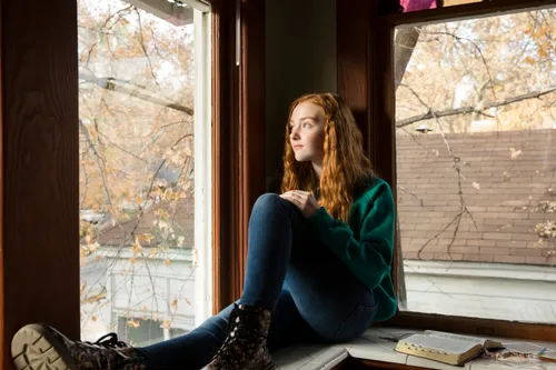 a young woman sitting by a window and looking outside