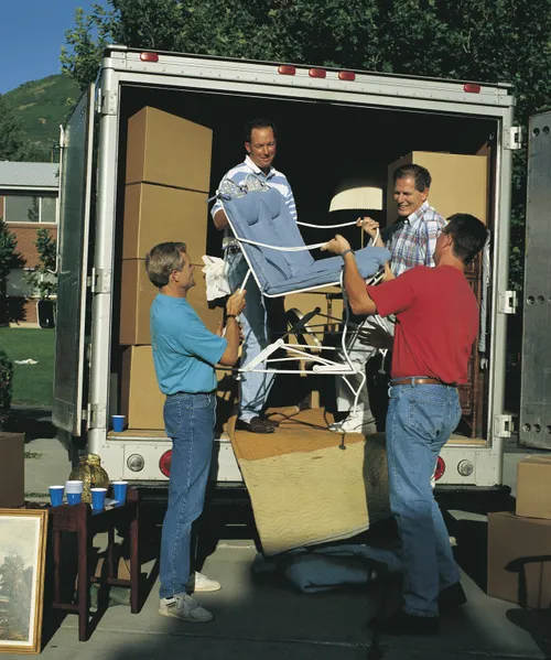 Four men work together to unload a large moving truck, which is filled with cardboard boxes and furniture.