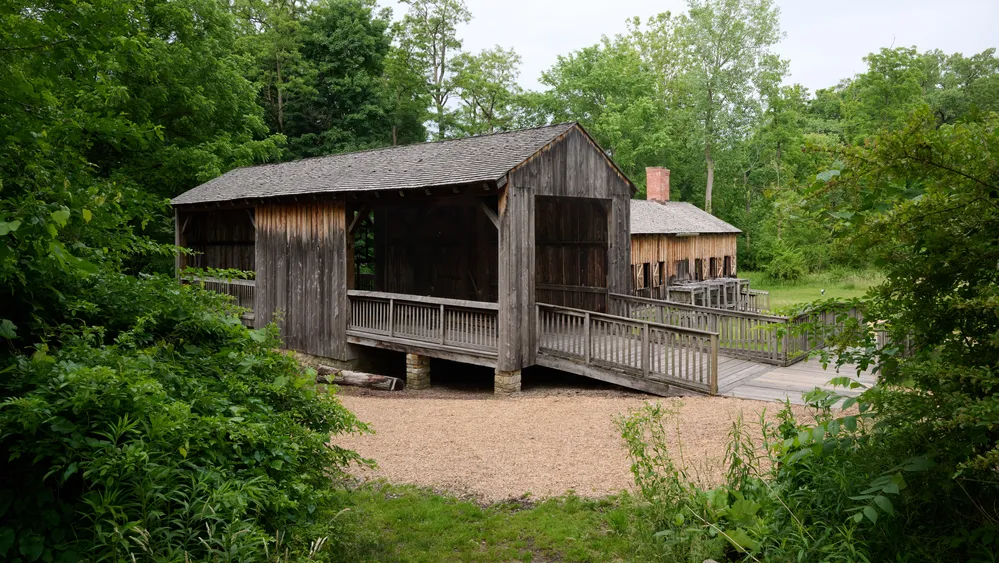 The saw mill. An open air building built from gray, weathered wood. A second building, the ashery, is visible behind.