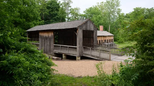 The saw mill. An open air building built from gray, weathered wood. A second building, the ashery, is visible behind.