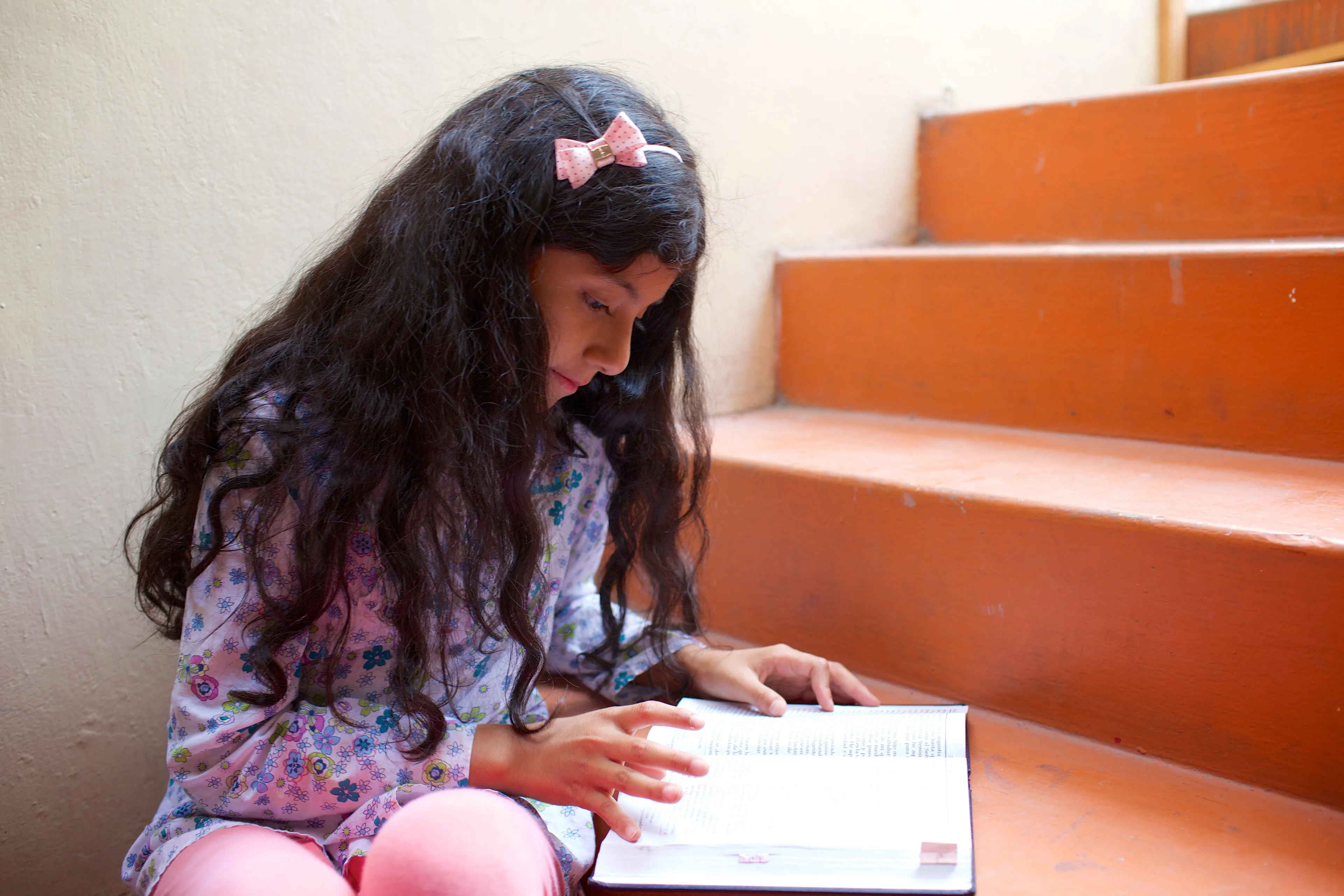 A young girl sits on the steps and reads her scriptures.