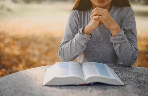 a woman folds her hands in prayer while reading the scriptures