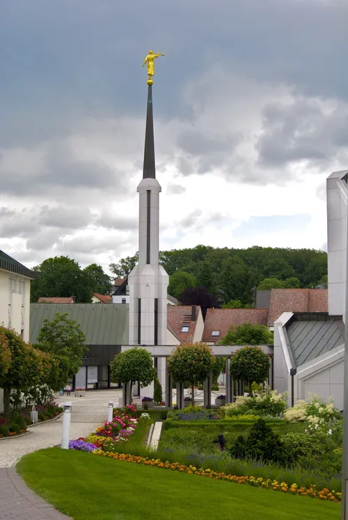 The spire next to the Frankfurt Germany Temple, with green lawns and colorful flowers in the foreground.