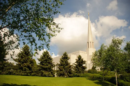 The spire of the Preston England Temple rising above the surrounding vegetation and trees on the temple grounds.