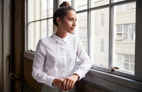 A woman stands by a windowsill and looks out the window