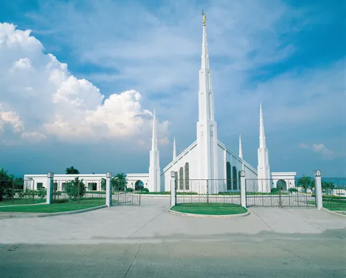 A view of the front gate entrance to the Manila Philippines Temple, with a blue sky and clouds in the distance.
