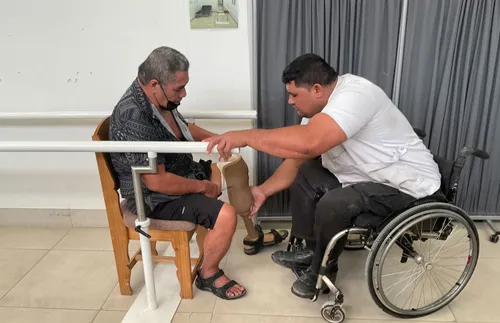 man in a wheelchair helping another man with a prosthetic leg