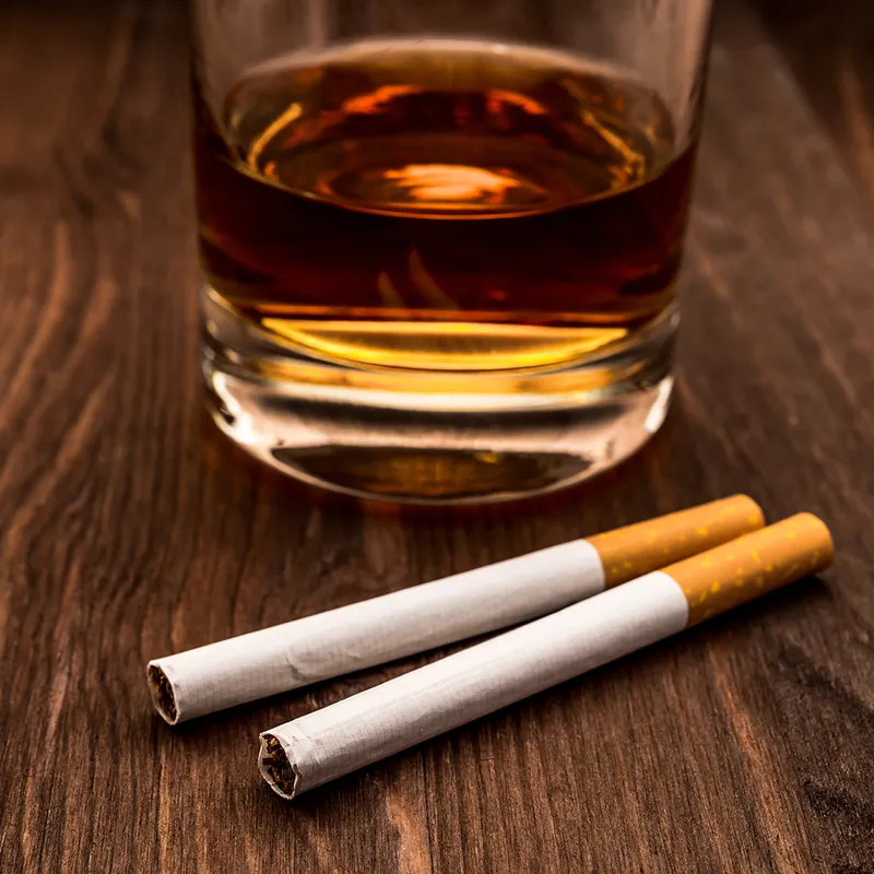 A glass of alcohol on a kitchen table with two unused cigarets one of the do nots of the word of wisdom