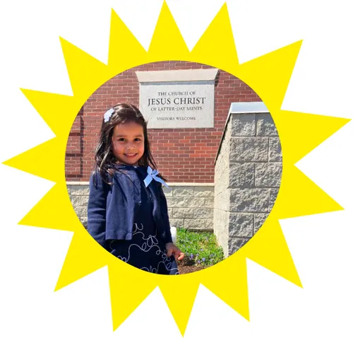 A young girl stands outside a meetinghouse in her Sunday dress.  She's stops on the sidewalk for a picture.