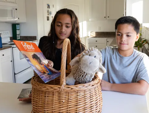 Girl and boy putting a Friend magazine and stuffed sheep toy in a basket
