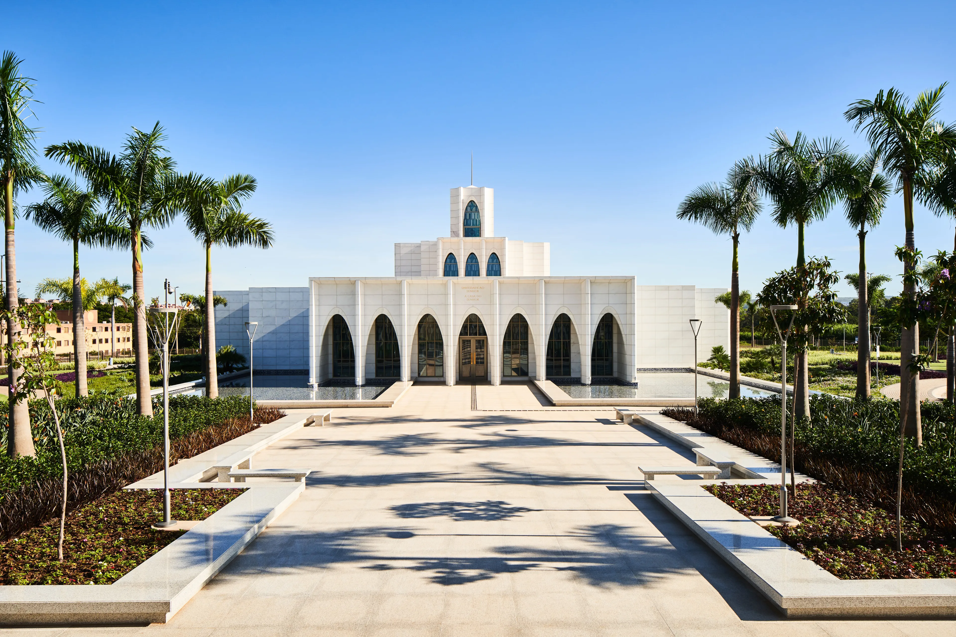 Exterior of the Brasilia Brazil Temple. It features the front of the temple, the entrance area, and trees nearby. Image was taken during the day.