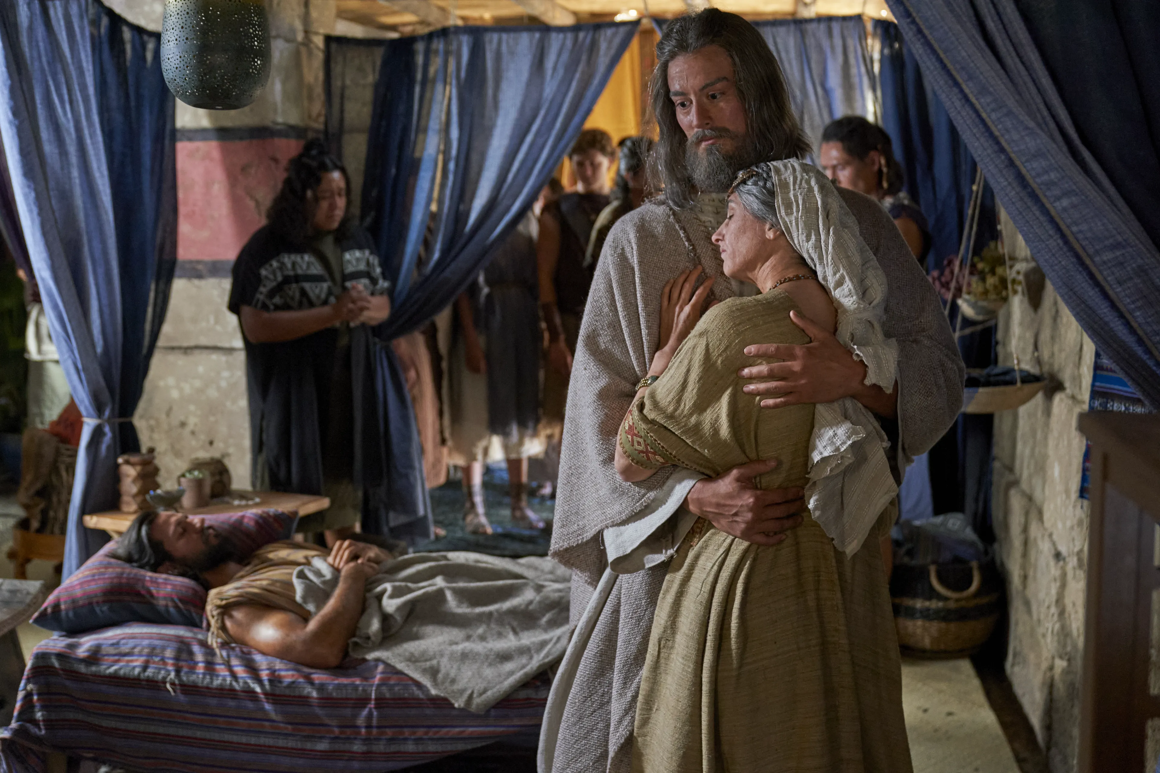 Alma the Elder holds his wife as Alma the Younger lays in bed, struck dumb.