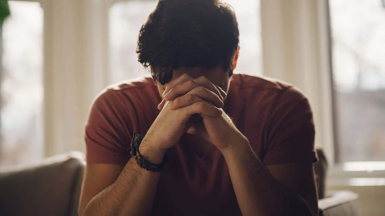 A man with interlocked hands kneels in prayer