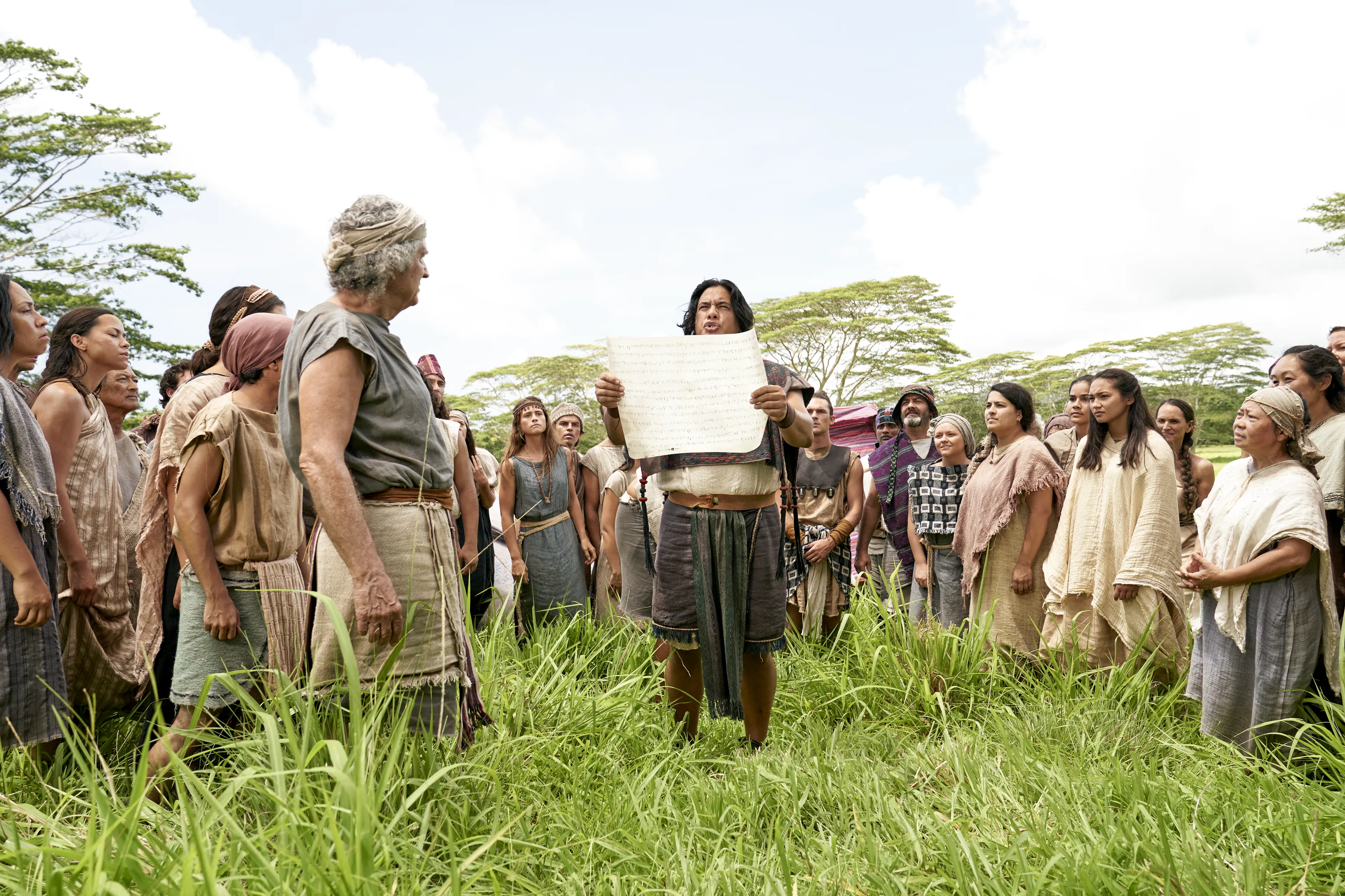 Men and women gather to listen to the teaching of King Benjamin as they are read from a parchment in the Land of Zarahemla.