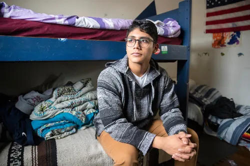 A young man sits on his bed and appears to be thinking about something.