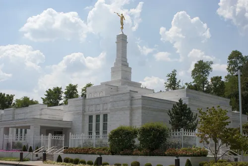 The Louisville Kentucky Temple on a bright day, with large green bushes and small pink flowers growing on the temple grounds.
