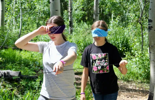 two blindfolded young women walking while holding on to a rope