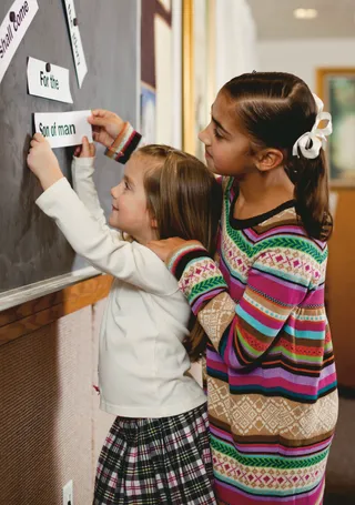 two girls putting word strips on chalkboard