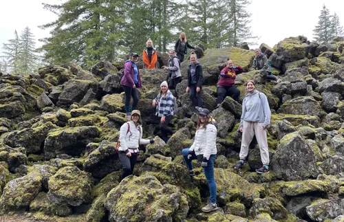 a group of young women and their leaders standing outdoors among some large rocks 