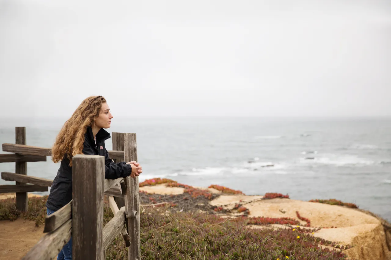 A woman leans on a railing above the seaside contemplating the gospel of Jesus Christ