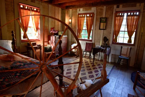 A large spinning wheel, a bed, a dresser, and several chairs in the house on the Smith family farm.