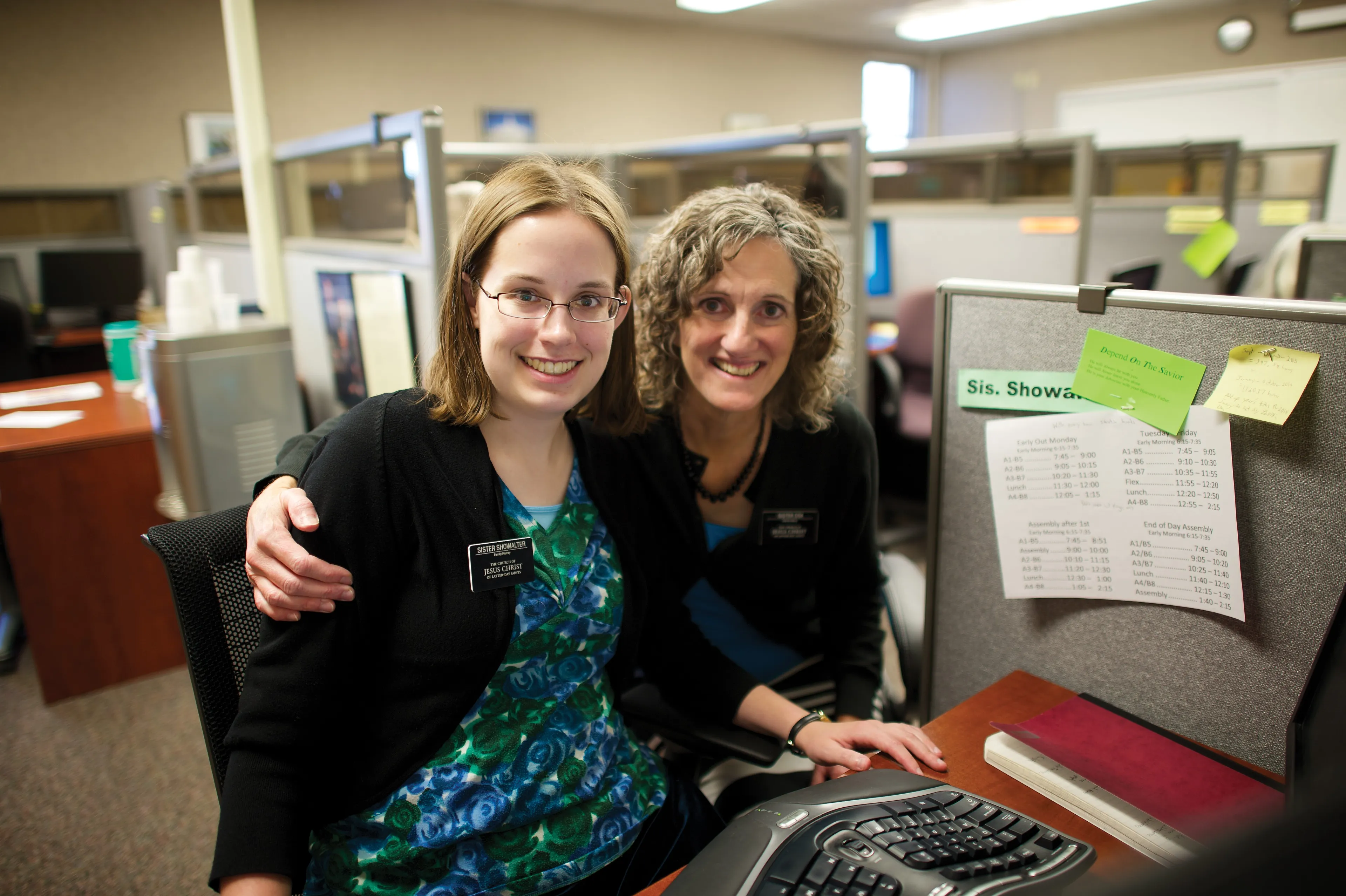 Two Church-service missionaries work together in an office at a computer.