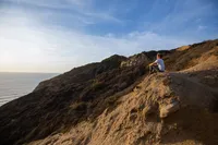 A woman sits on a cliffside contemplating the blessings of Jesus Christ and forgiveness