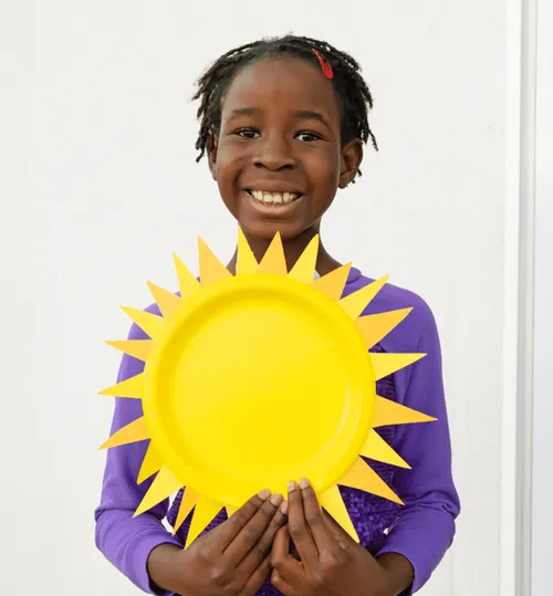 Child holding a sun made from yellow paper