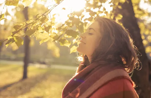Young adult woman with eyes closed by fall trees