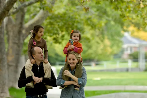 Parents with two girls on their shoulders walking in a park.